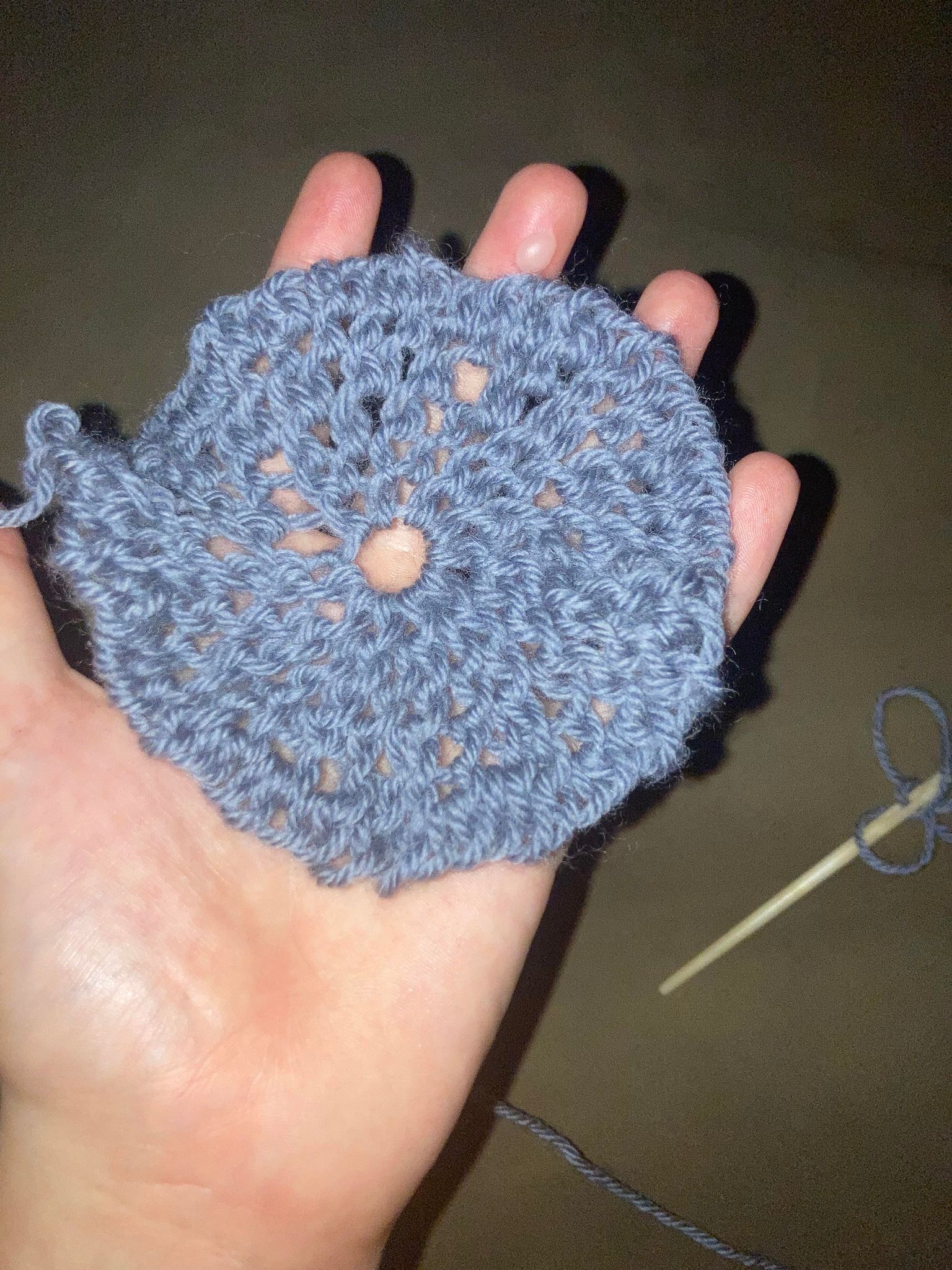 A hand holding a small circle of netting made of blue wool.